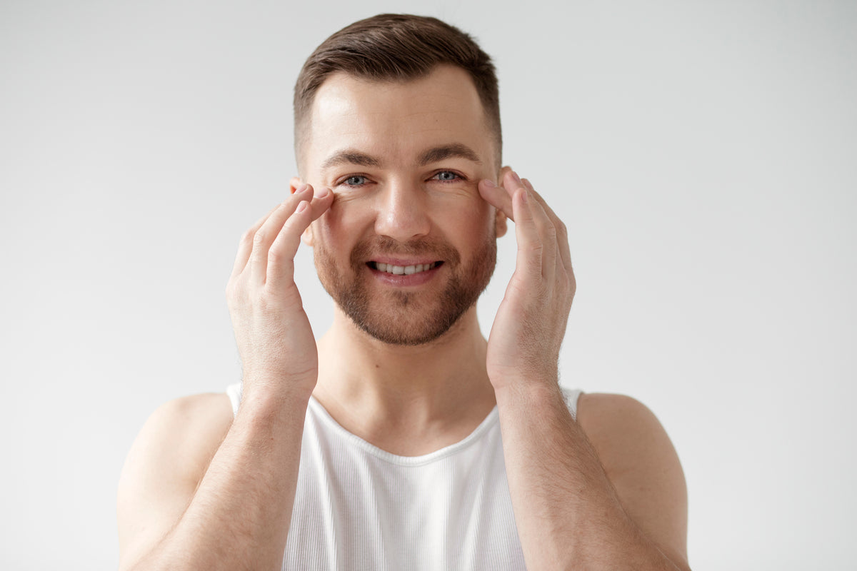 Man gently applying eye cream under his eyes, smiling and looking refreshed.