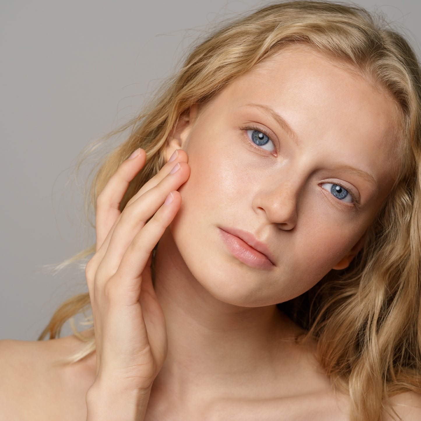 Close-up of a woman with blonde hair gently touching her face, showcasing healthy, clear skin.