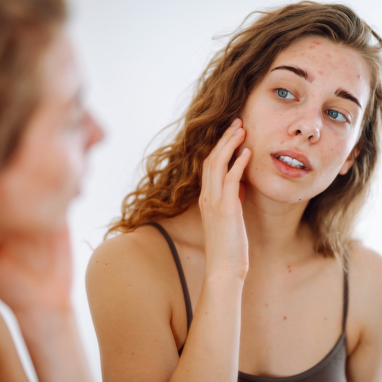 Woman examining her complexion in a mirror, focusing on blemishes.