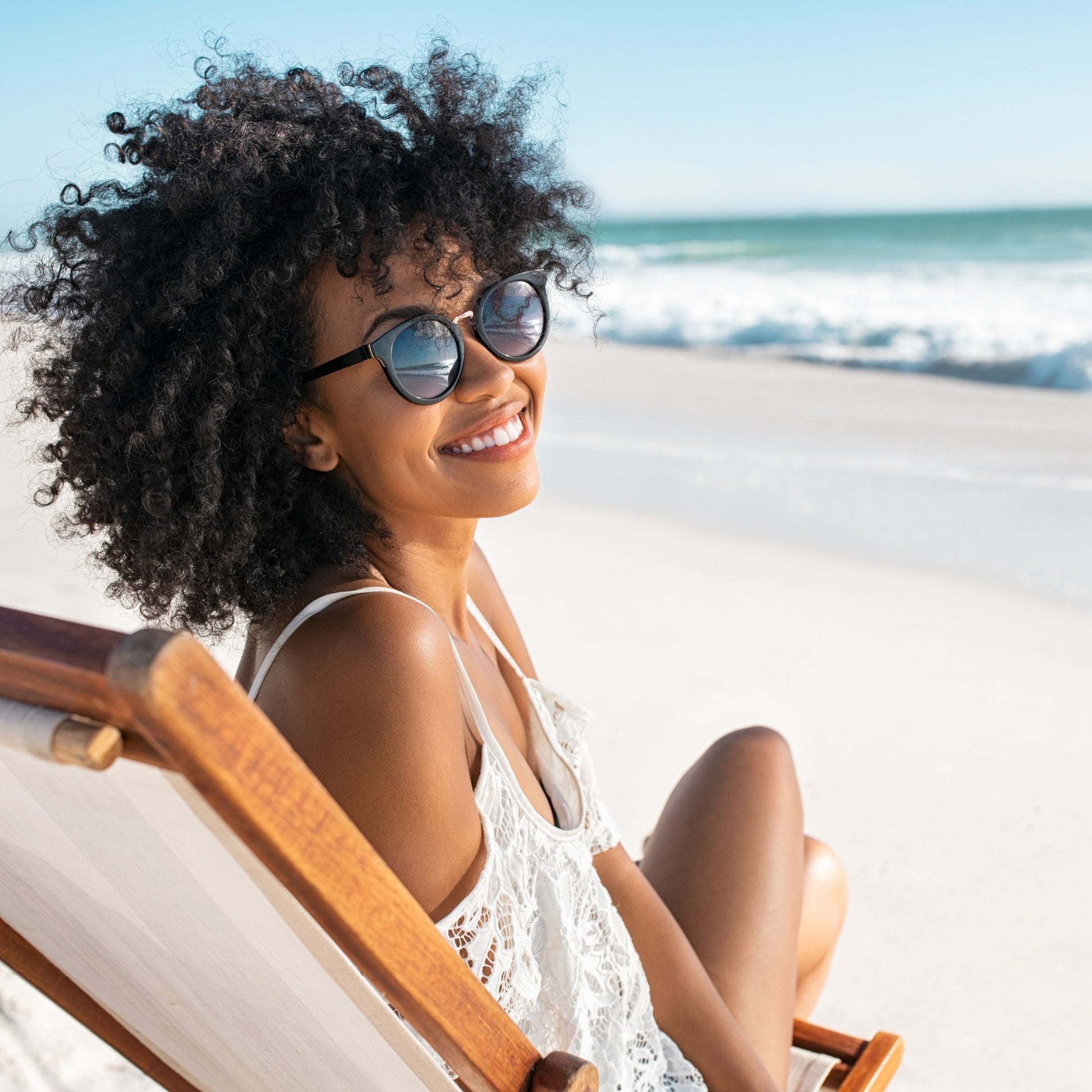 Smiling woman relaxing in beach chair, wearing sunglasses, ocean in background.