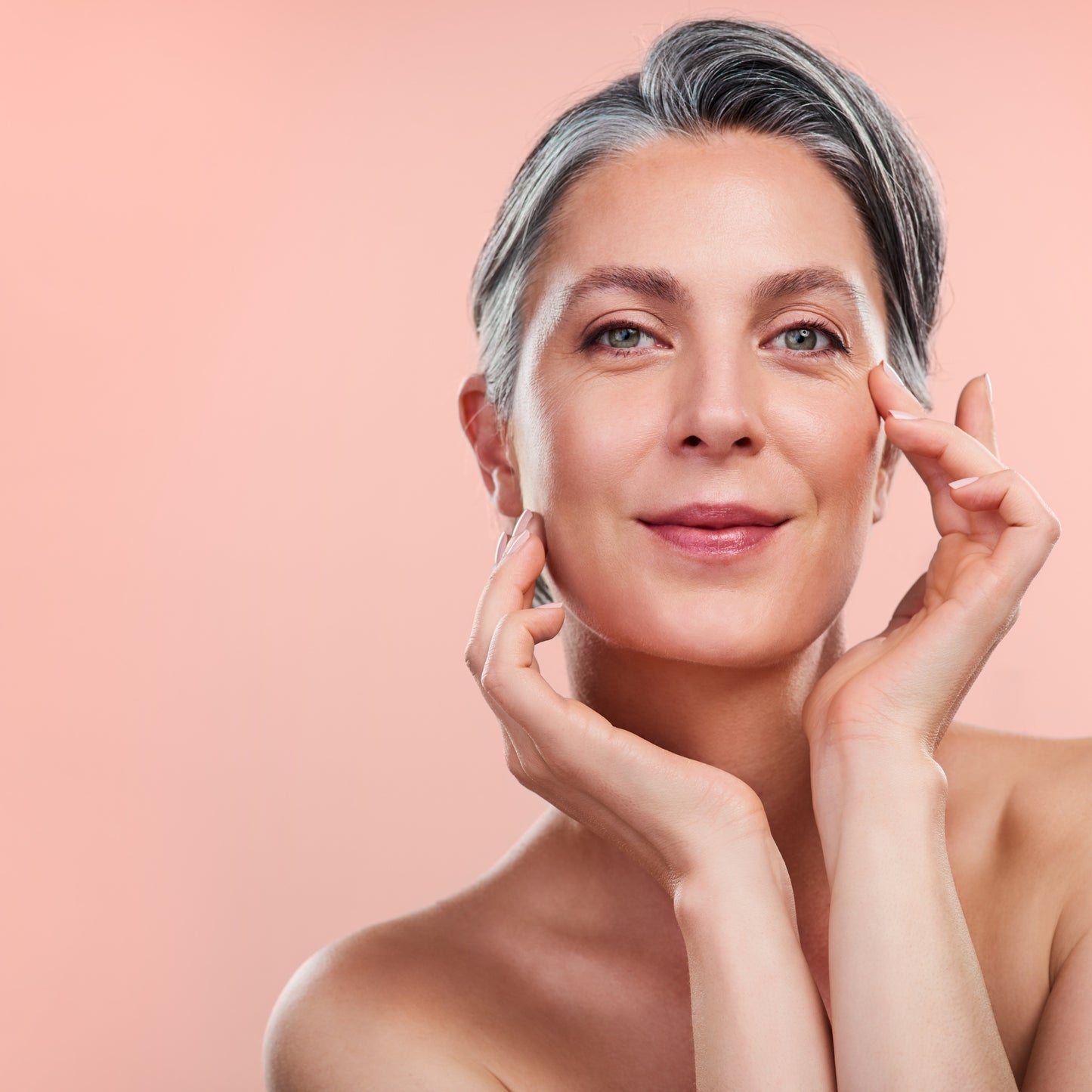 Woman with combination skin gently touching her face against a pale pink background.