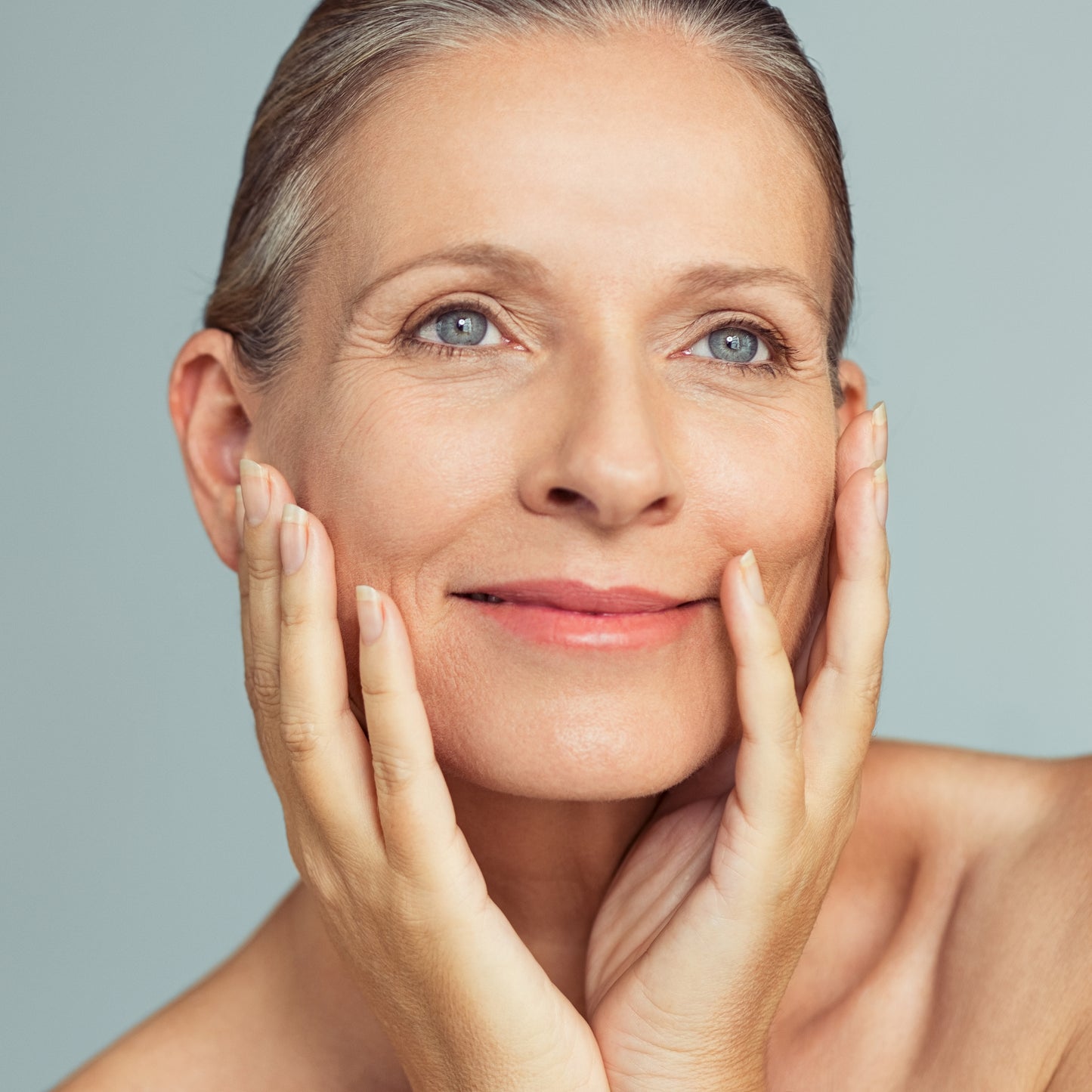 Close-up of a woman gently touching her face, showcasing healthy, radiant skin against a soft blue backdrop.