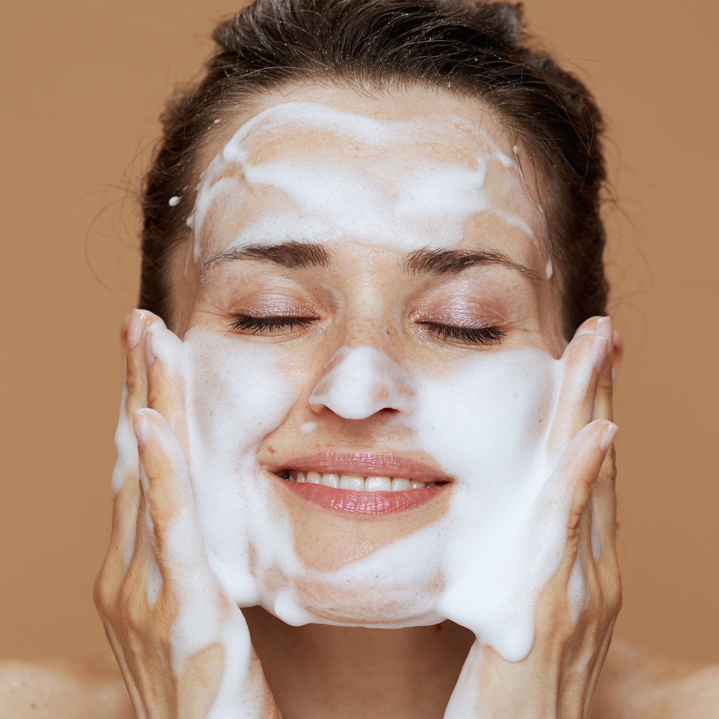 Woman cleansing face with rich, creamy foam cleanser, eyes closed.
