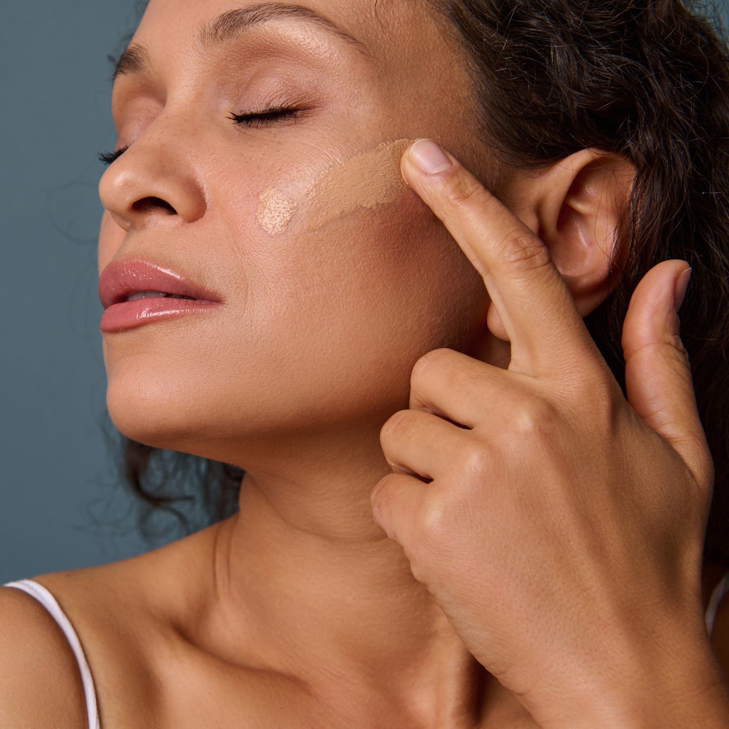 Woman applying beige BB cream to her cheek, close-up view.