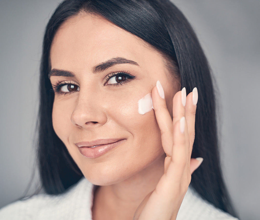 Woman applying creamy white facial balm, close-up.