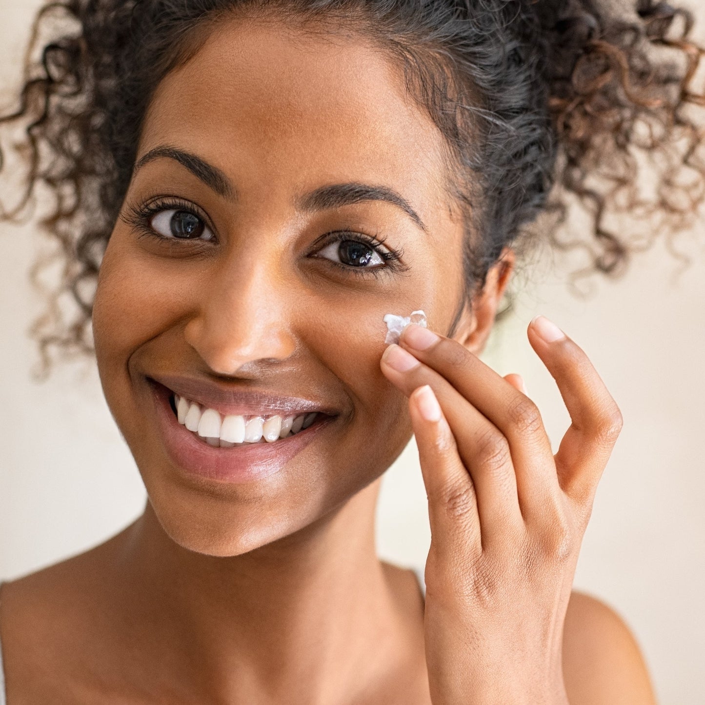 Smiling woman applying creamy moisturizer to her face.