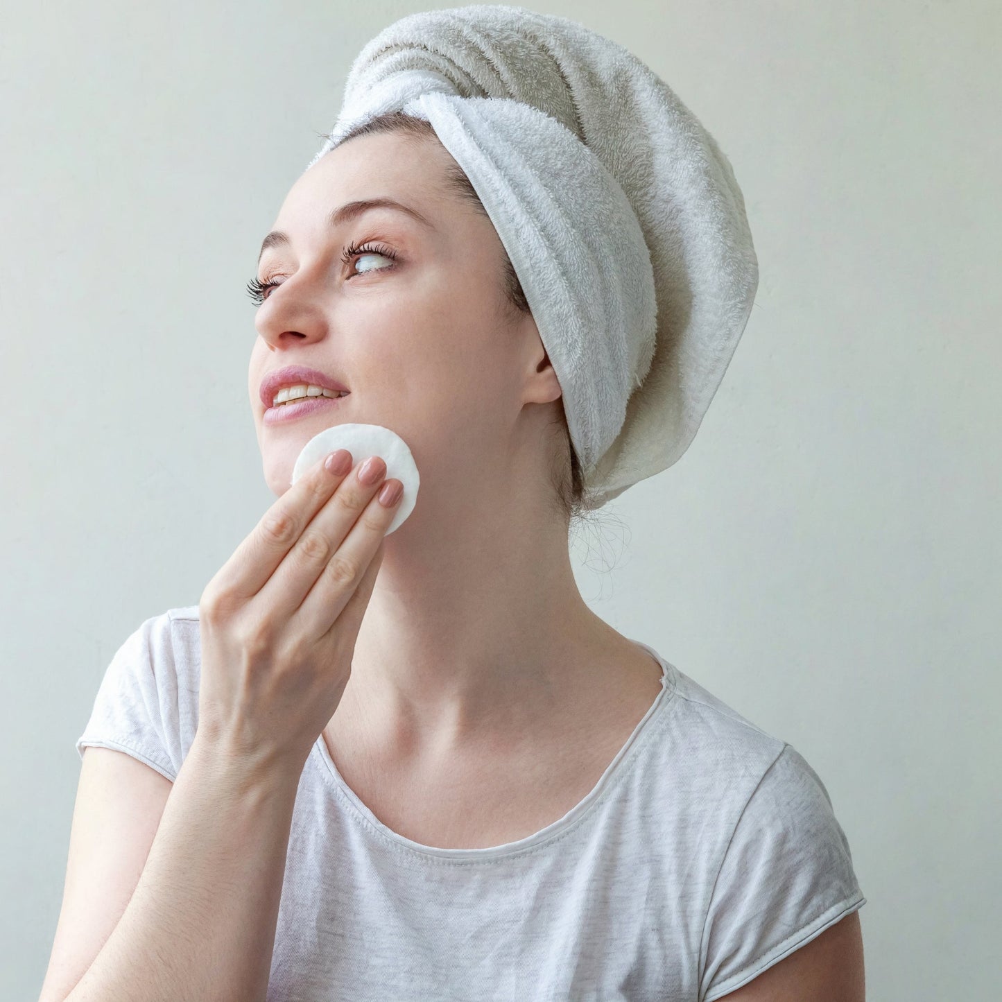 Woman using a cleansing pad on her face, post-shower skincare routine.