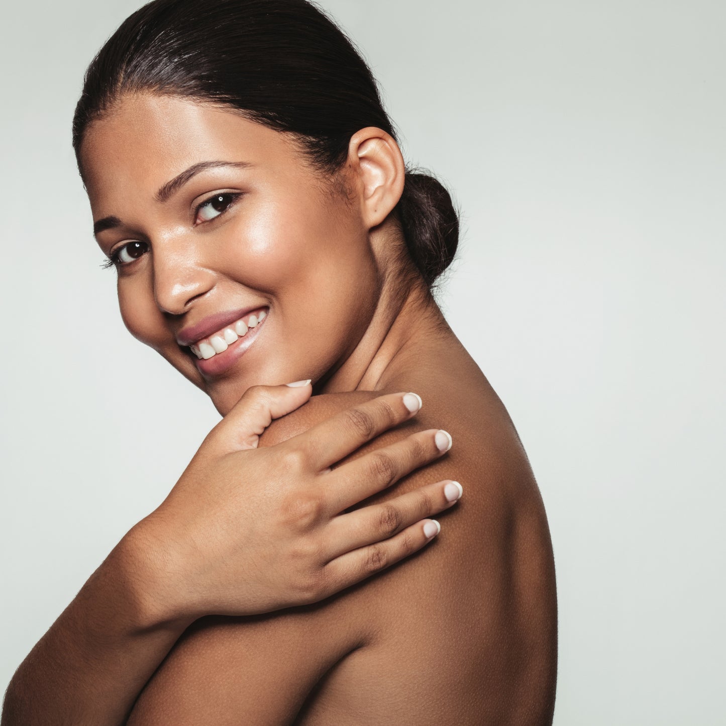 Smiling woman with radiant skin, showcasing healthy, smooth complexion against a neutral background.