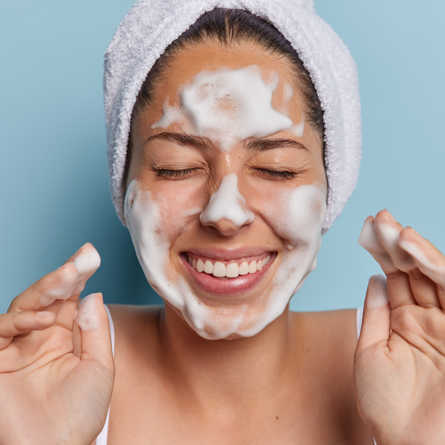 Close-up of a smiling woman with a rich, creamy cleanser lather on her face, showcasing its airy texture.