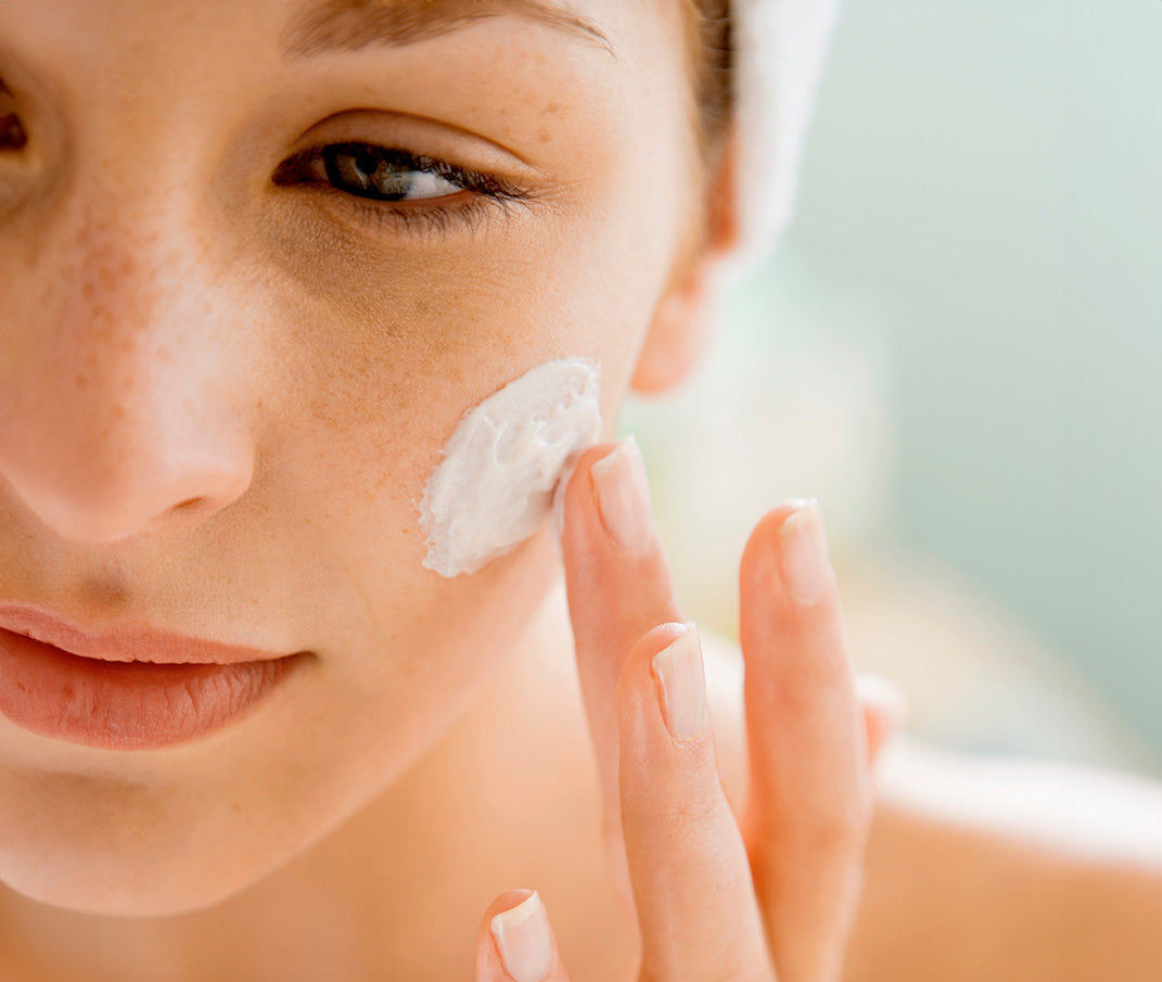 Woman applying creamy, white balm to her cheek.