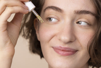 Close-up of a woman smiling as she applies a drop of facial serum near her eye with a dropper.