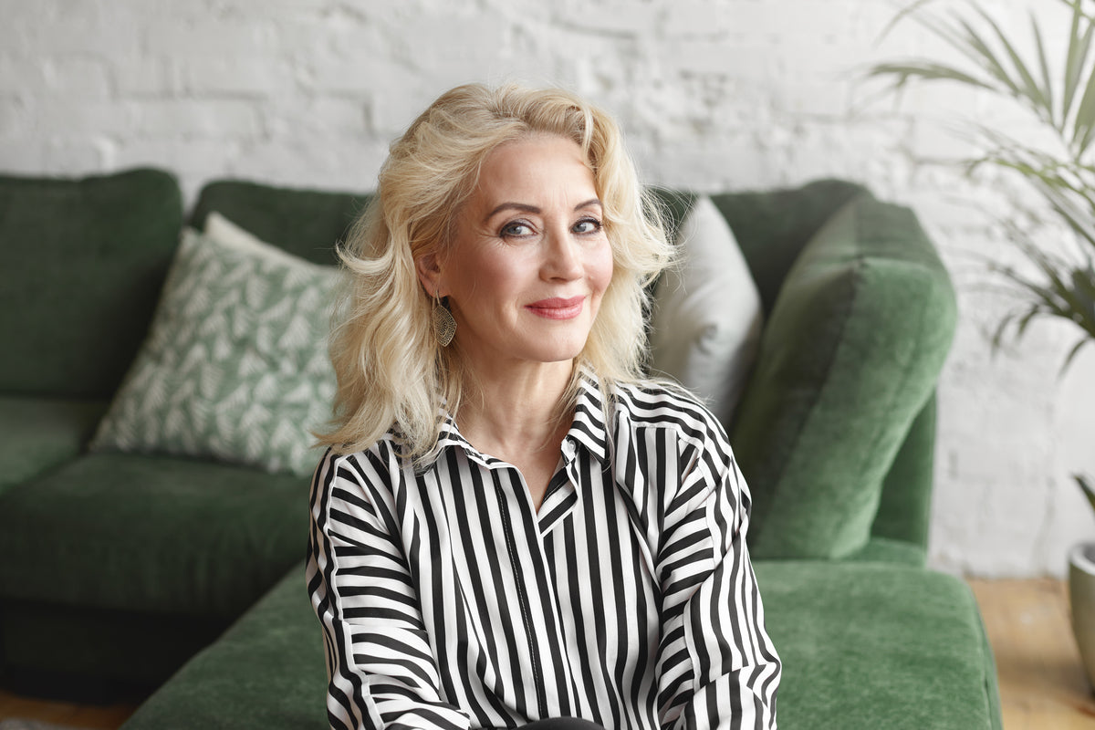 Dermatologist-recommended skincare routine illustrated by a confident middle-aged woman with healthy, radiant skin sitting in a bright, modern living space.