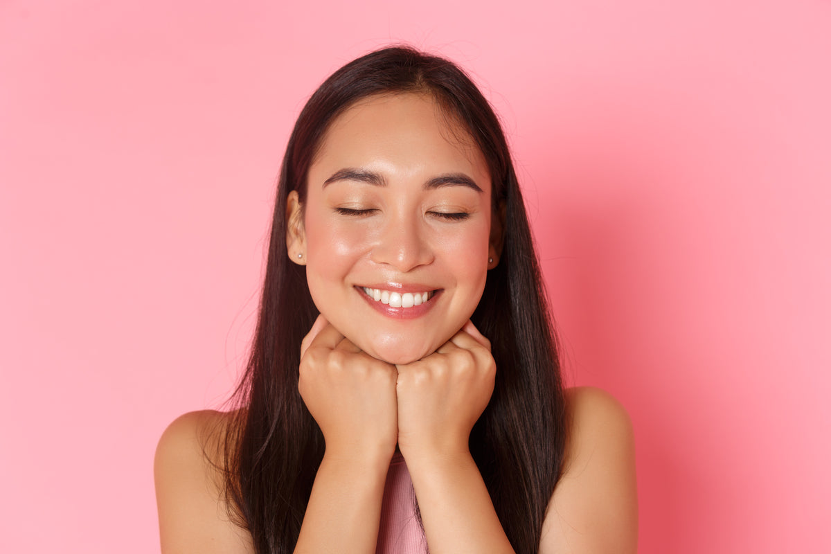 Smiling woman with smooth, glowing-looking skin against a pink background, representing results often associated with using a chemical peel kit.