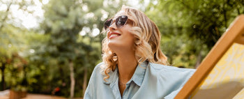 A smiling, clear-skinned woman in sunglasses relaxes outdoors.