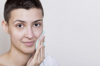 Woman with short hair gently pressing a soft facial cleansing pad to her cheek, illustrating a gentle approach to blemish control for sensitive skin.