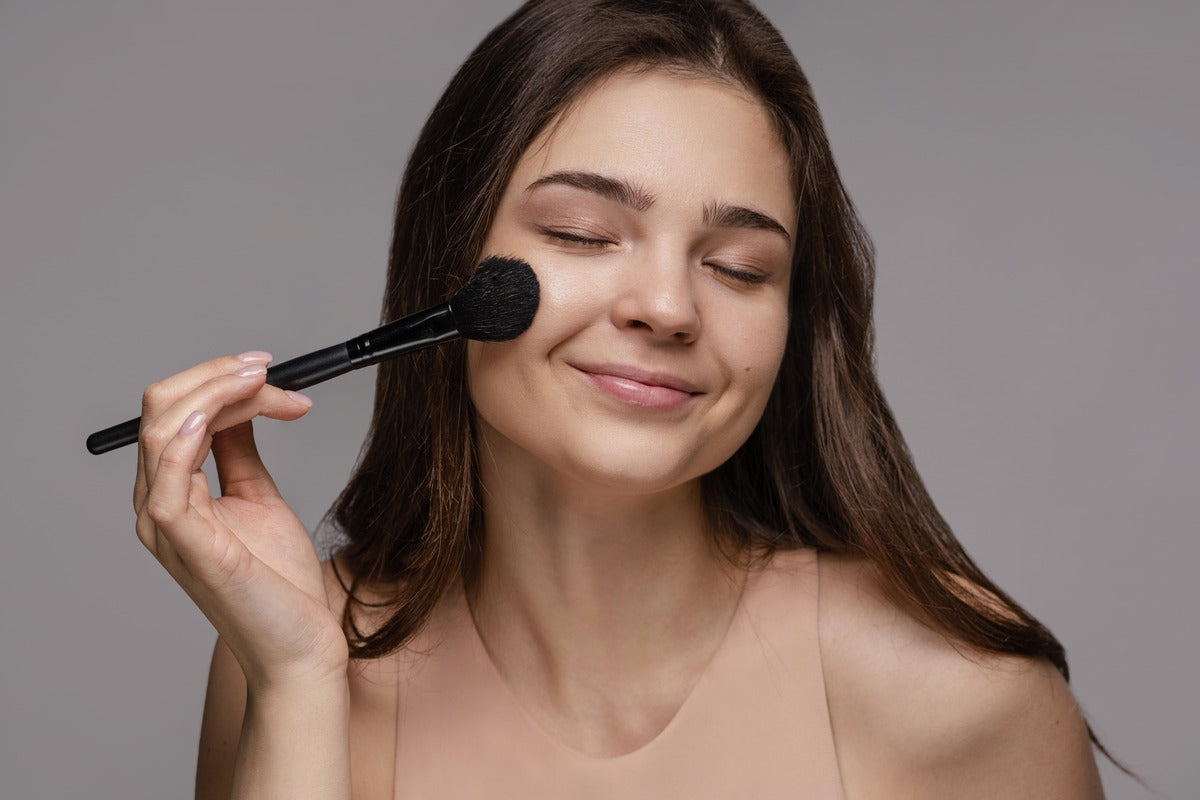 Woman applying powder SPF with a makeup brush to demonstrate how to reapply sunscreen over makeup without disrupting foundation.