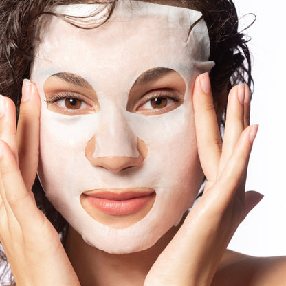 Close-up of woman applying a sheet face mask.
